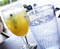 Two glasses on a table: one with orange juice and mint leaves, and another with water and ice cubes, suggesting a healthier lifestyle choice often encouraged in hypnotherapy treatments for alcoholism.