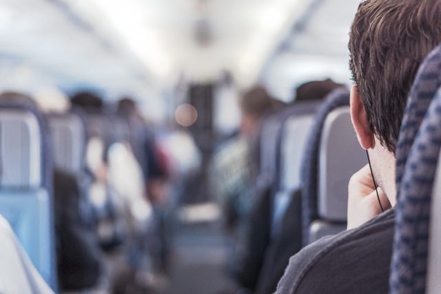 Passenger view inside an airplane cabin showing the backs of seats and other passengers ahead.