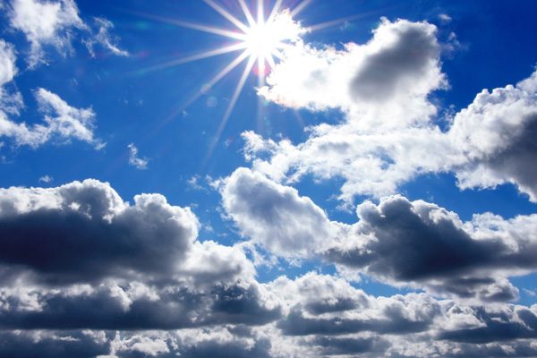 Blue sky with puffy clouds and a bright sun creating rays of light.