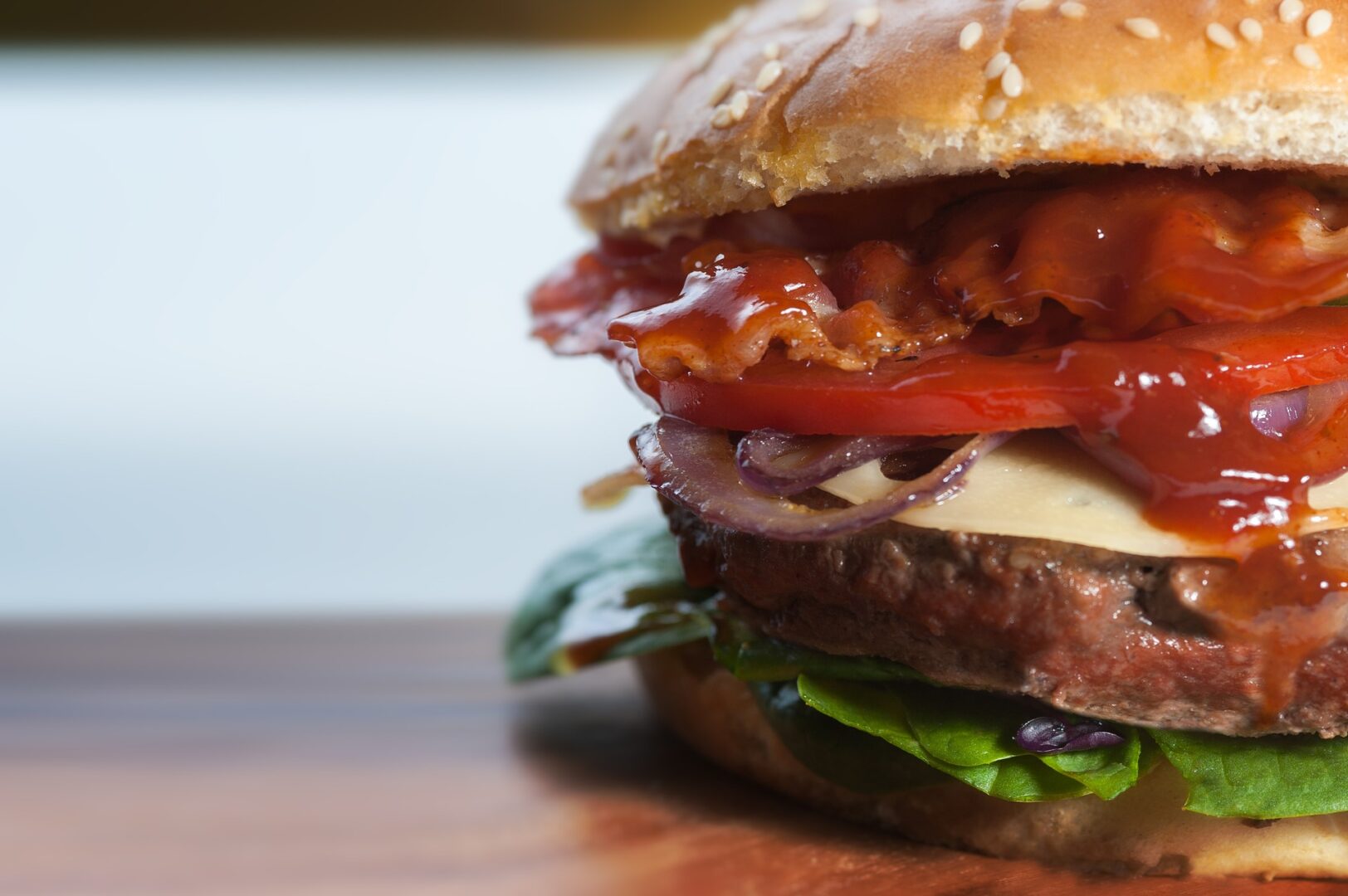 Close-up of a juicy burger with lettuce, tomato, onions, cheese, and a glossy, rich sauce on a sesame seed bun.