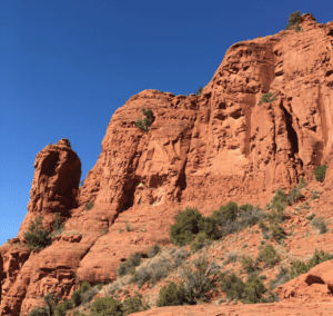 Red sandstone cliffs under a clear blue sky with sparse green vegetation at the base, reminiscent of the tranquil scenes often discussed in hypnotherapy sessions in San Mateo, CA.