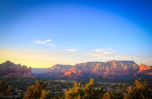 Panoramic view of Sedona's red rock formations at sunset with vibrant sky and foreground greenery, perfect for relaxing before a hypnotherapy session in San Mateo, CA.