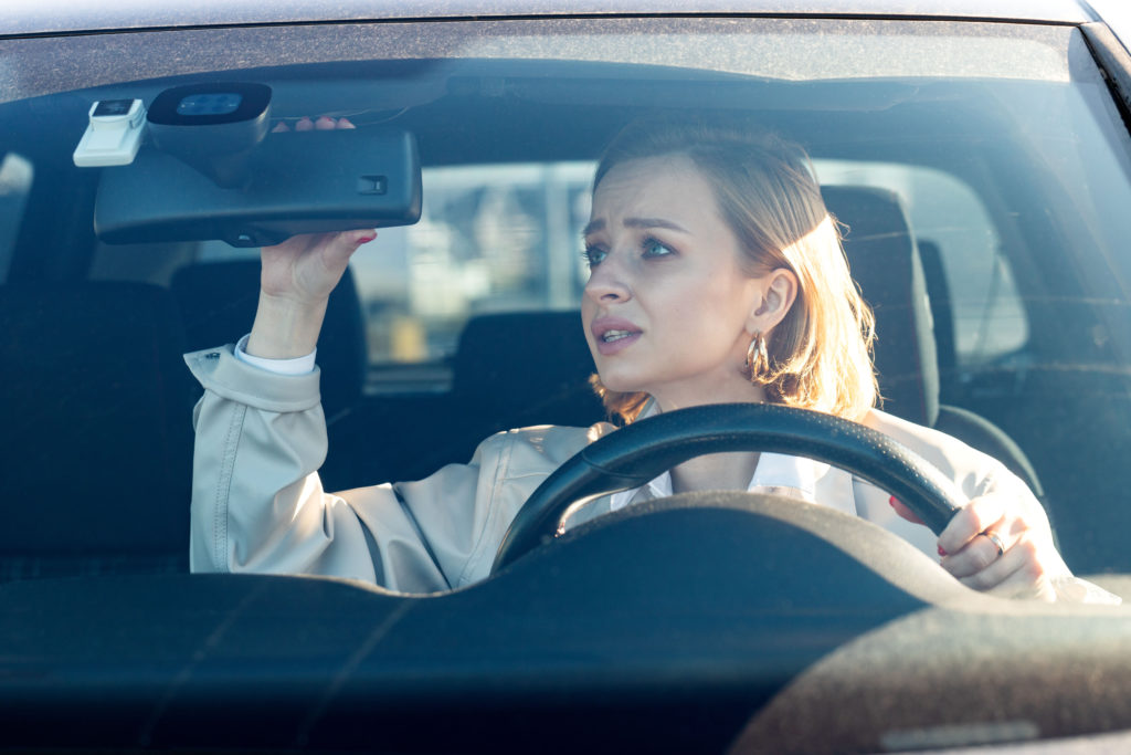 Woman adjusting rearview mirror while sitting in the driver's seat of a car after a hypnotherapy session to help with driving anxiety.