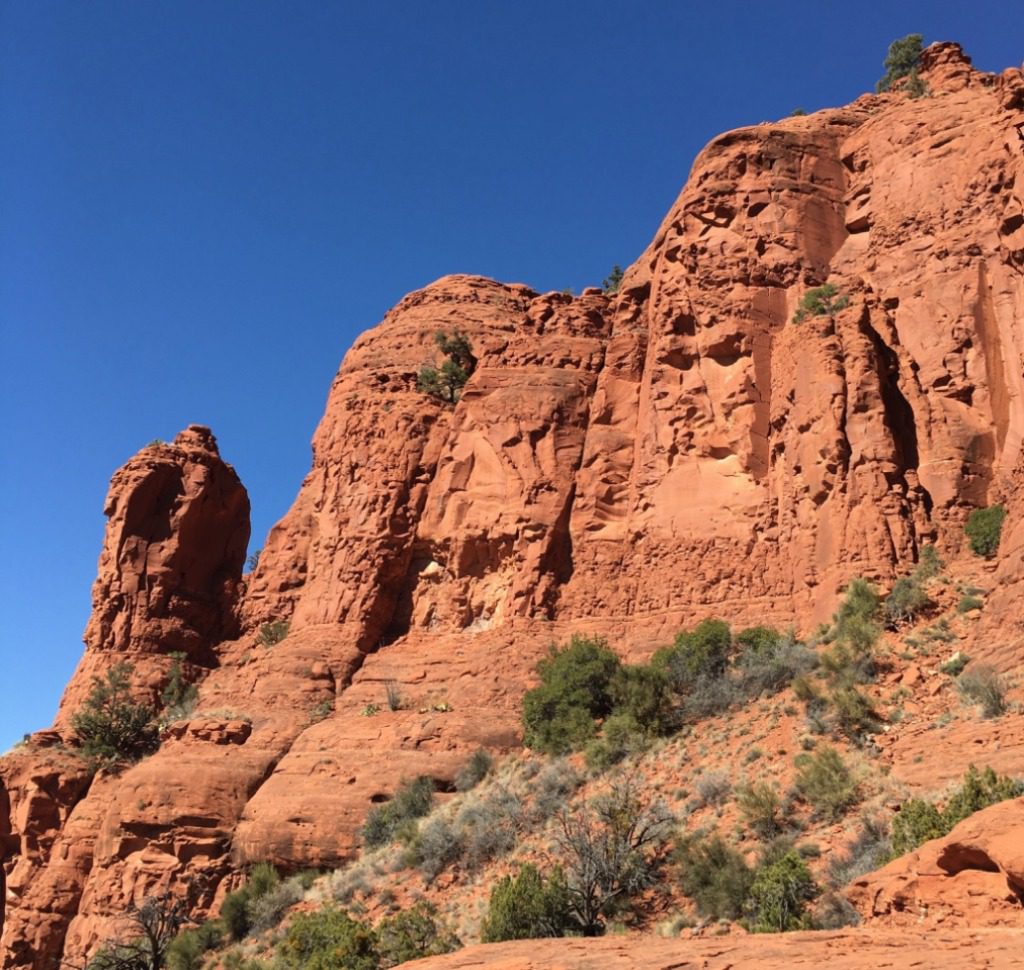 Red sandstone cliffs under a clear blue sky, with sparsely vegetated desert terrain at the base.