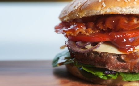 Close-up of a juicy burger with lettuce, tomato, onions, cheese, and a glossy, rich sauce on a sesame seed bun.